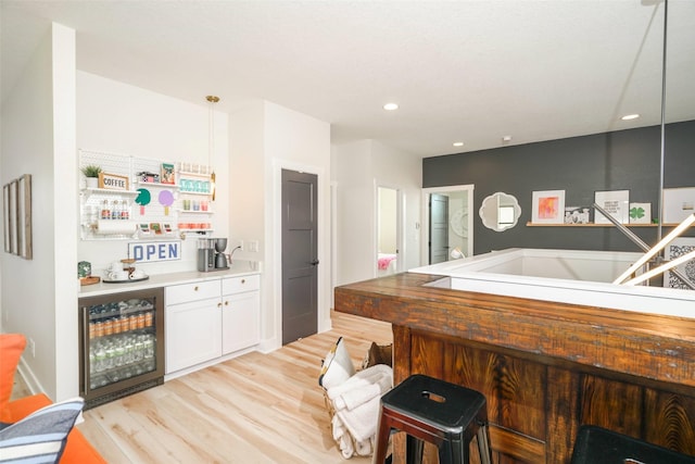 bar featuring white cabinetry, pendant lighting, beverage cooler, and light hardwood / wood-style flooring