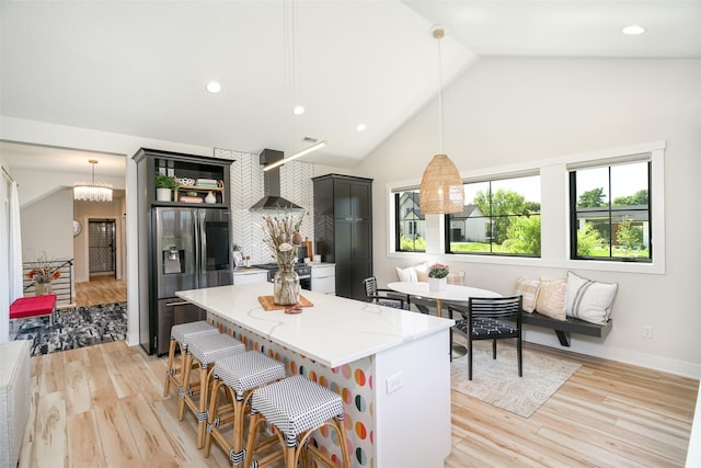 kitchen with light stone countertops, wall chimney exhaust hood, stainless steel appliances, pendant lighting, and light hardwood / wood-style flooring