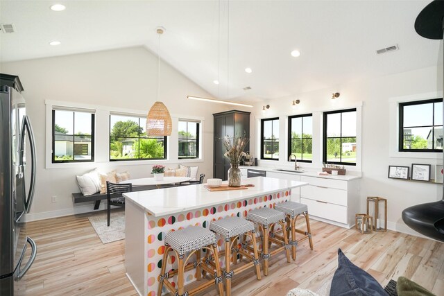 kitchen with stainless steel fridge, white cabinets, pendant lighting, and light wood-type flooring