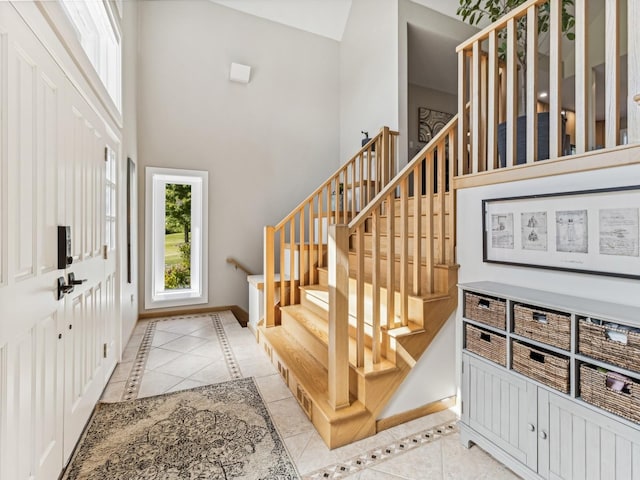 foyer featuring stairs, a high ceiling, baseboards, and light tile patterned flooring