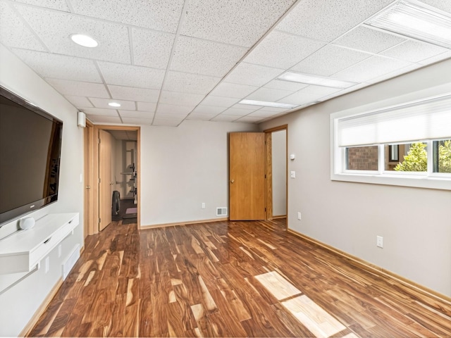 unfurnished living room featuring a paneled ceiling, visible vents, baseboards, and wood finished floors