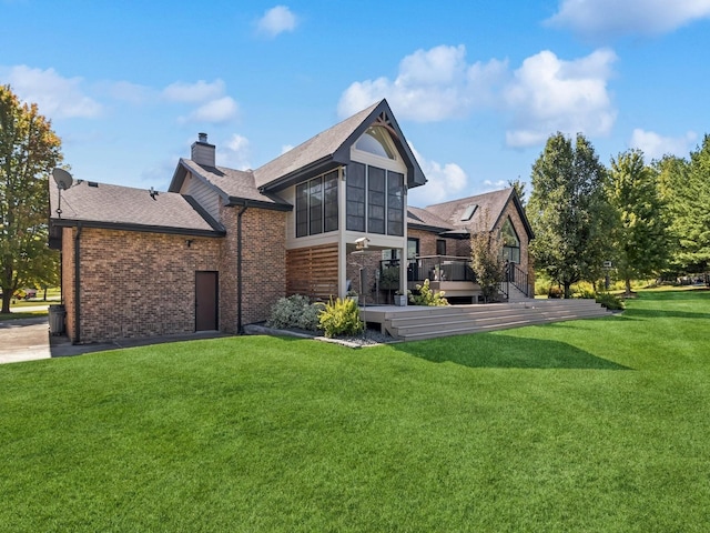 rear view of property featuring a chimney, a deck, a lawn, and brick siding