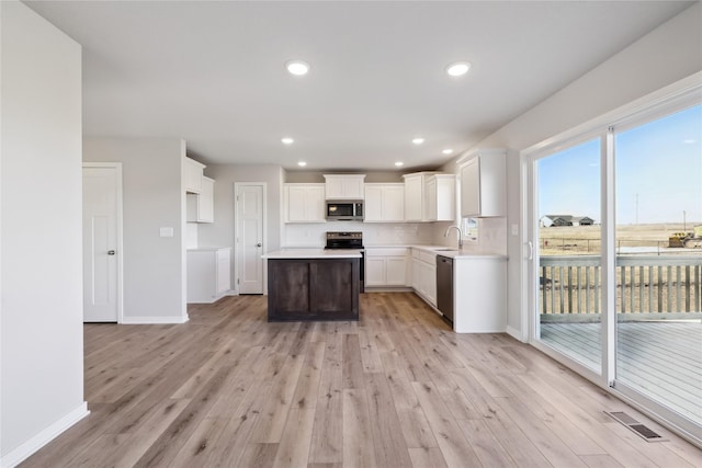 kitchen featuring sink, appliances with stainless steel finishes, white cabinetry, light hardwood / wood-style floors, and a kitchen island