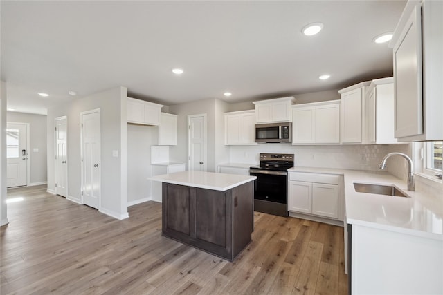 kitchen with a kitchen island, sink, white cabinets, light hardwood / wood-style floors, and stainless steel appliances