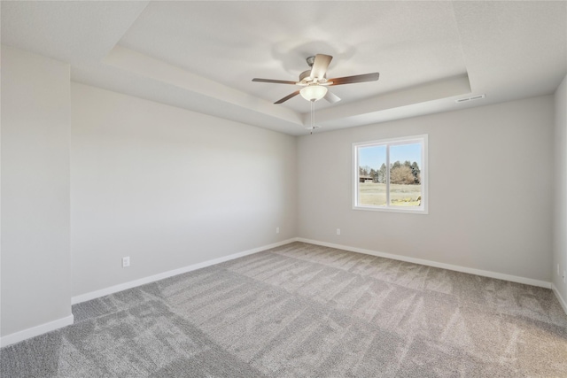 carpeted spare room with a tray ceiling and ceiling fan