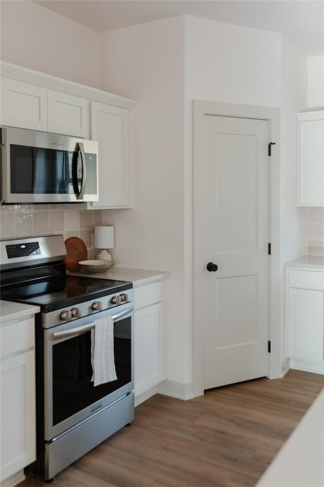 kitchen with appliances with stainless steel finishes, backsplash, light hardwood / wood-style floors, and white cabinetry