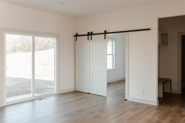 spare room with a barn door, light hardwood / wood-style floors, and a healthy amount of sunlight