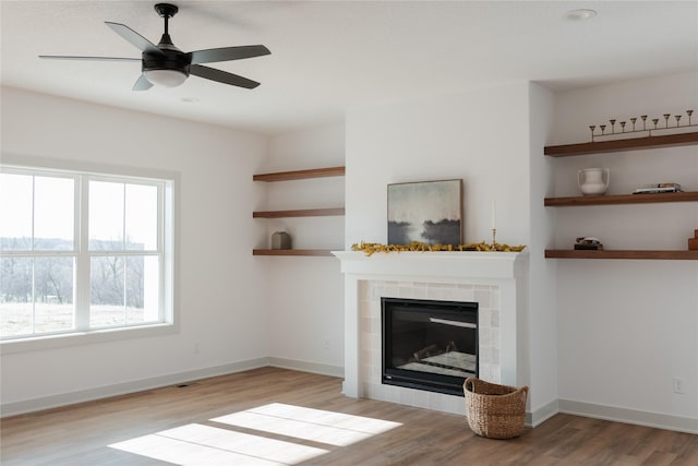 unfurnished living room with ceiling fan, a tile fireplace, and light hardwood / wood-style flooring