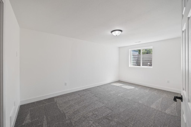 spare room featuring dark carpet and baseboards