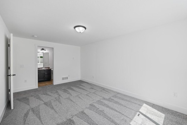 unfurnished bedroom featuring carpet, visible vents, baseboards, a sink, and ensuite bathroom