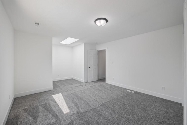 carpeted empty room featuring visible vents, baseboards, and a skylight