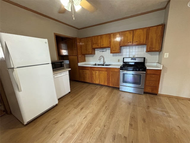 kitchen with sink, crown molding, light wood-type flooring, appliances with stainless steel finishes, and tasteful backsplash