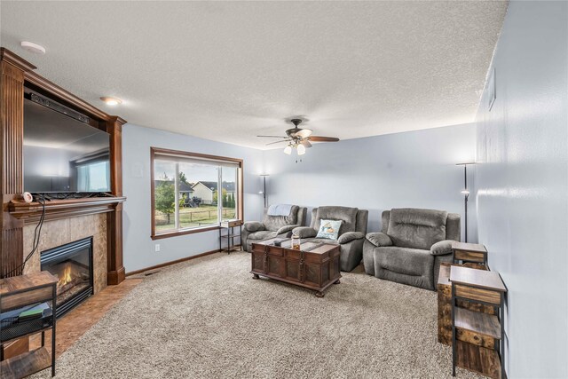 carpeted living room with a tile fireplace, ceiling fan, and a textured ceiling