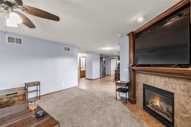 living room featuring ceiling fan, a textured ceiling, light carpet, and a tiled fireplace