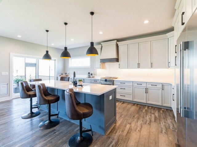 kitchen with white cabinetry, decorative light fixtures, an island with sink, premium range hood, and dark hardwood / wood-style floors