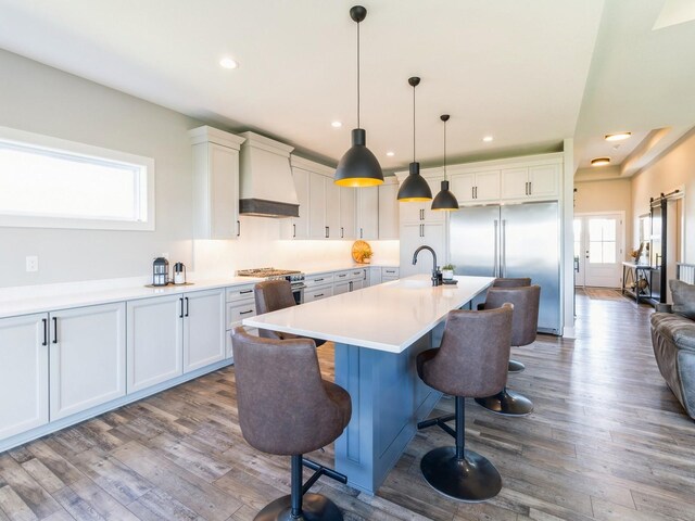 kitchen featuring a center island with sink, custom range hood, a kitchen bar, hardwood / wood-style flooring, and white cabinetry