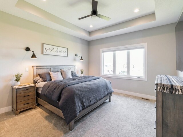 carpeted bedroom with ceiling fan and a raised ceiling