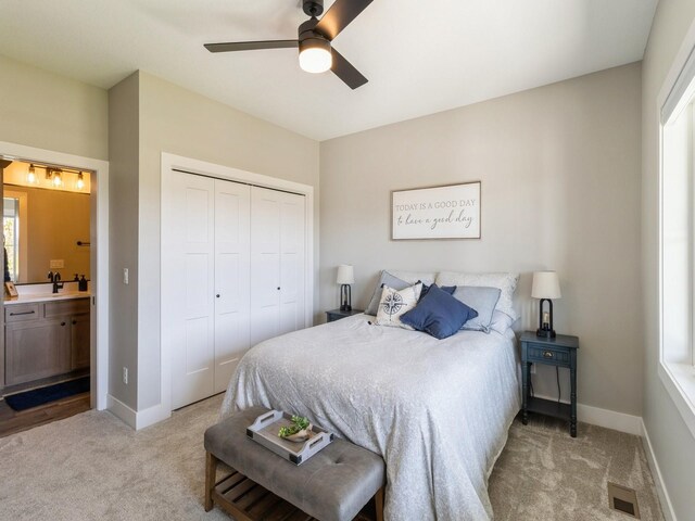 bedroom with a closet, ceiling fan, ensuite bathroom, and light carpet