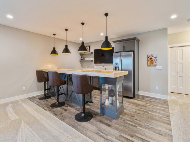 kitchen featuring light wood-type flooring, a kitchen breakfast bar, gray cabinetry, and stainless steel fridge with ice dispenser