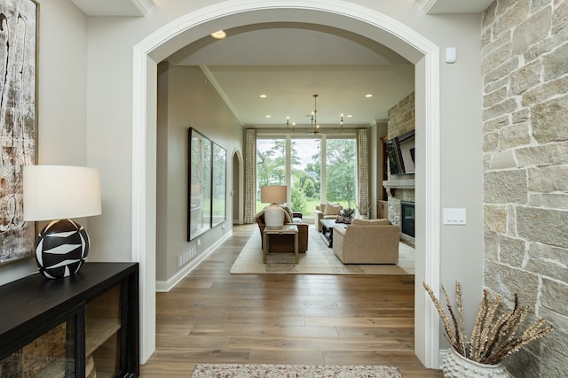 living room featuring crown molding, light hardwood / wood-style flooring, and a stone fireplace