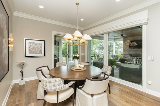 dining space featuring light wood-type flooring, ceiling fan with notable chandelier, crown molding, and a brick fireplace