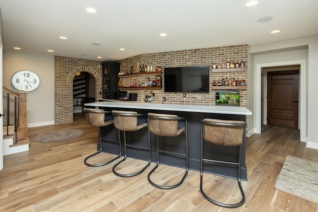 bar with light hardwood / wood-style floors and brick wall