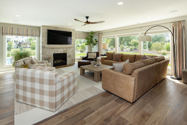 living room featuring hardwood / wood-style floors, ceiling fan, and a stone fireplace