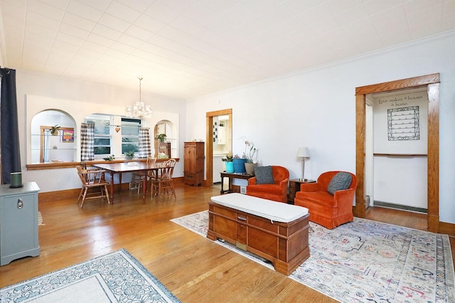 living room with ornamental molding, a chandelier, and light wood-type flooring