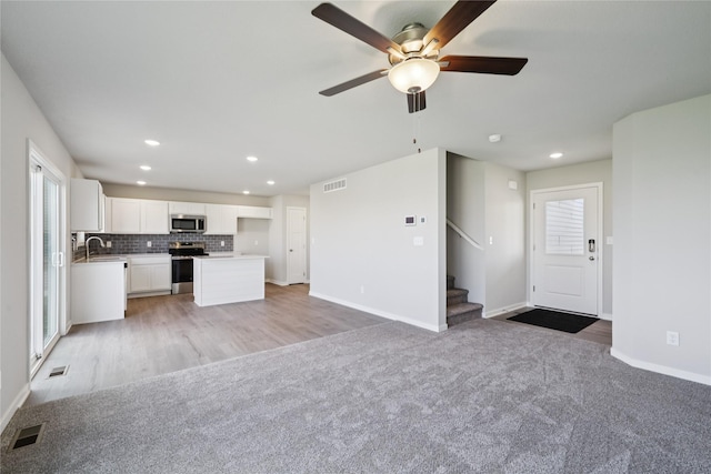 805 3rd St NW, Bondurant, IA 50035 - unfurnished living room with light colored carpet, recessed lighting, a ceiling fan, stairway, and light wood-style floors