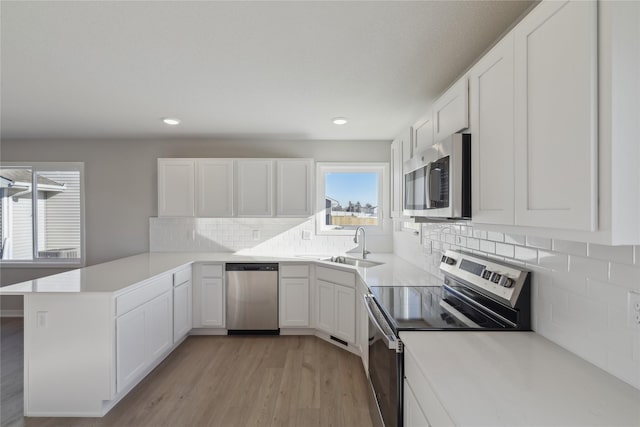 kitchen with kitchen peninsula, light hardwood / wood-style flooring, white cabinets, appliances with stainless steel finishes, and sink