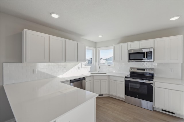 kitchen with light hardwood / wood-style flooring, stainless steel appliances, tasteful backsplash, white cabinets, and sink