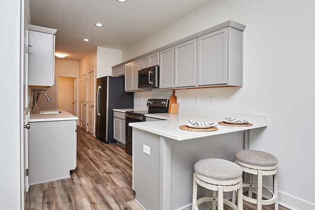 kitchen featuring gray cabinetry, sink, appliances with stainless steel finishes, a kitchen bar, and kitchen peninsula