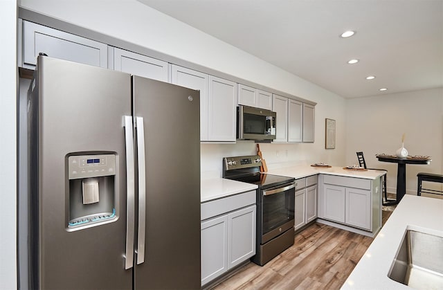 kitchen with kitchen peninsula, stainless steel appliances, gray cabinets, and light hardwood / wood-style flooring