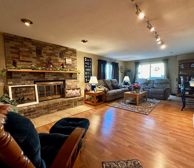 living room featuring hardwood / wood-style floors, a textured ceiling, track lighting, and a brick fireplace