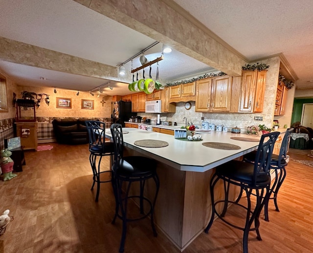 kitchen with rail lighting, black fridge, light hardwood / wood-style floors, a textured ceiling, and a breakfast bar area