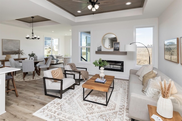 living room with a raised ceiling, wooden ceiling, ceiling fan with notable chandelier, and light wood-type flooring