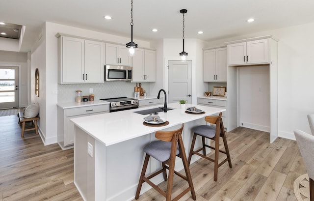 kitchen with stainless steel appliances, a kitchen island with sink, light hardwood / wood-style floors, and sink