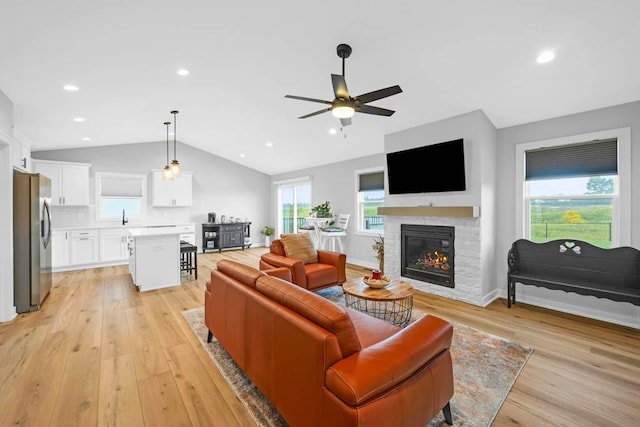 living room featuring ceiling fan, a stone fireplace, light wood-type flooring, and vaulted ceiling