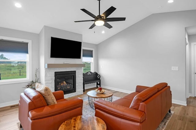 living room featuring ceiling fan, a fireplace, vaulted ceiling, and light wood-type flooring