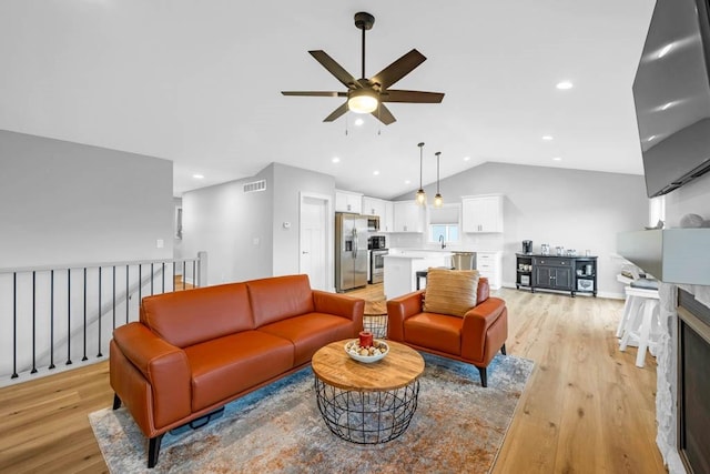 living room with ceiling fan, light hardwood / wood-style flooring, lofted ceiling, and sink