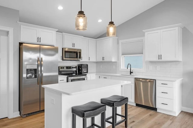 kitchen with a center island, lofted ceiling, white cabinets, sink, and appliances with stainless steel finishes