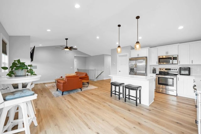 kitchen featuring a center island, lofted ceiling, hanging light fixtures, white cabinetry, and stainless steel appliances