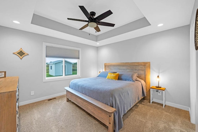 bedroom featuring a raised ceiling, ceiling fan, and light carpet