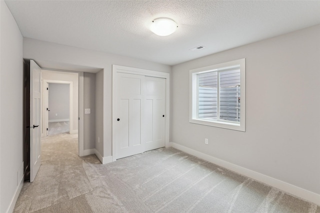 unfurnished bedroom featuring light colored carpet, a textured ceiling, and a closet