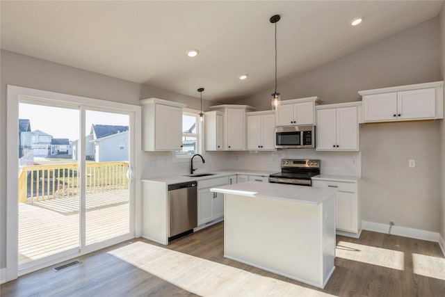 kitchen featuring stainless steel appliances, decorative light fixtures, white cabinets, a kitchen island, and lofted ceiling