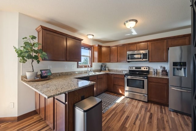 kitchen with a peninsula, appliances with stainless steel finishes, light stone counters, and wood finished floors