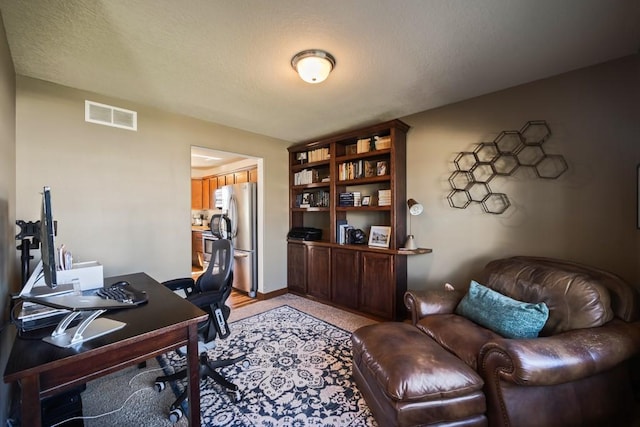 office area with baseboards, visible vents, and a textured ceiling