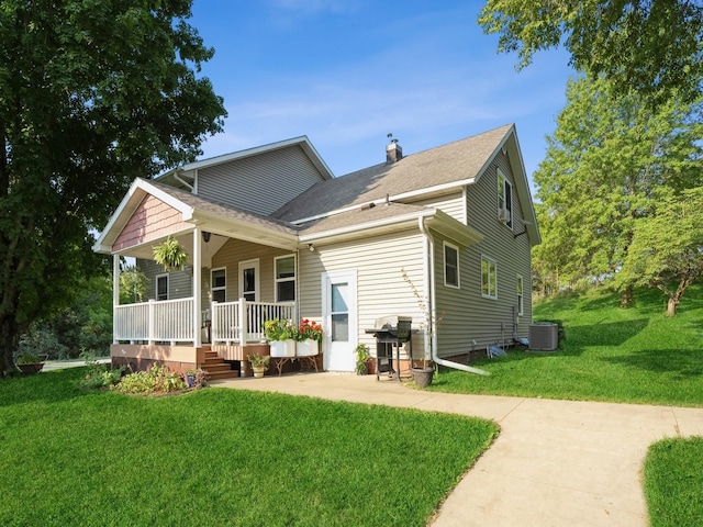 rear view of property with a porch, cooling unit, a shingled roof, a lawn, and a chimney