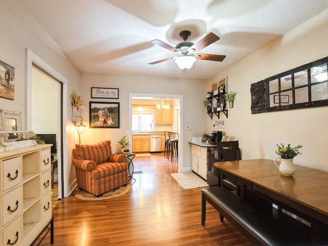 living area featuring a textured ceiling, wood finished floors, and ceiling fan with notable chandelier