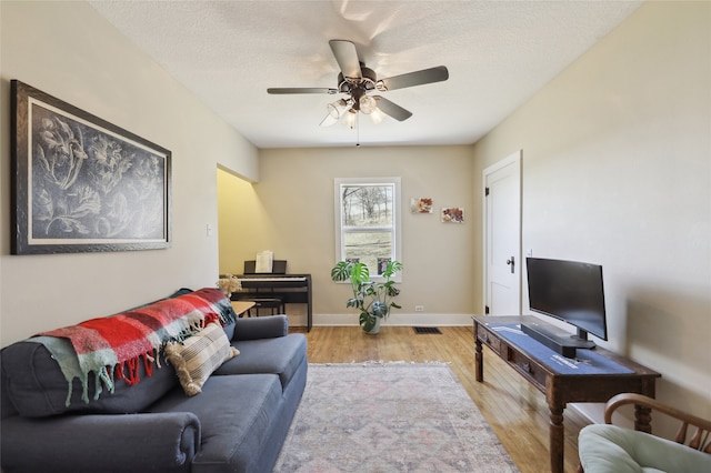 living room with ceiling fan, a textured ceiling, wood finished floors, visible vents, and baseboards